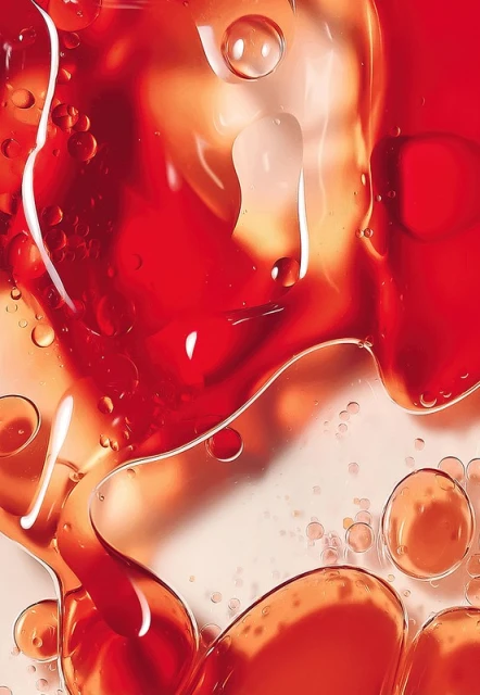 Macro shot of abstract oil and water mixture creating dynamic textures, fluid shapes, and vibrant red-orange color gradients on a bright backdrop.