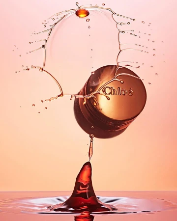 Chloe perfume bottle captured with high-speed photography, showing the collision of water droplets in a studio setting with pink background.