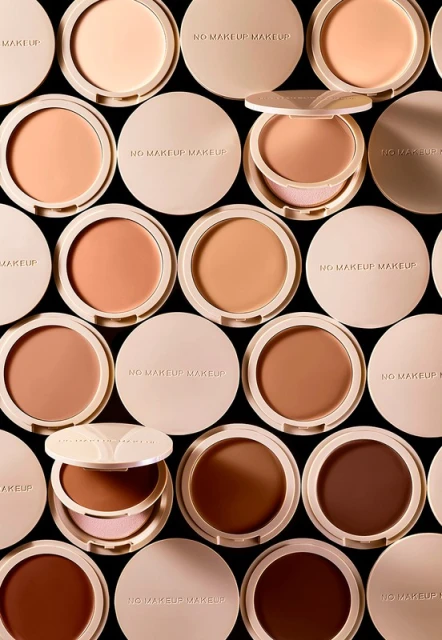 Overhead shot of arranged pressed powder makeup compacts in a variety of skin tones, some open, showcasing a range of colors.