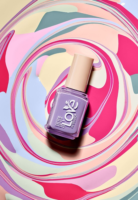 Overhead shot of purple Essie nail polish bottle on swirling pastel background. Beauty product photography of cosmetic bottle.