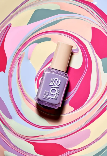 Overhead shot of purple Essie nail polish bottle on swirling pastel background. Beauty product photography of cosmetic bottle.