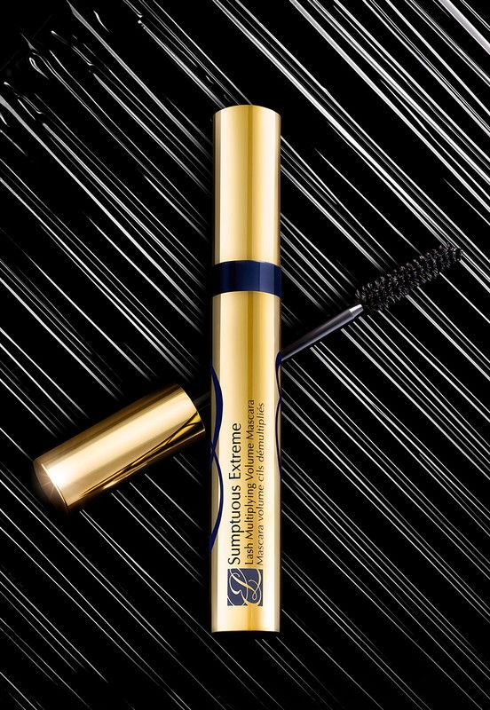 Close-up of gold Estee Lauder Sumptuous Extreme mascara tube and wand on black surface with streaks, beauty, cosmetics, and makeup concept.