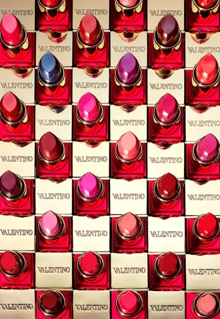 Cosmetic display showcasing a variety of Valentino lipsticks in red and gold packaging, arranged in a structured grid pattern.