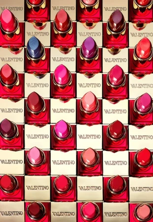 Cosmetic display showcasing a variety of Valentino lipsticks in red and gold packaging, arranged in a structured grid pattern.