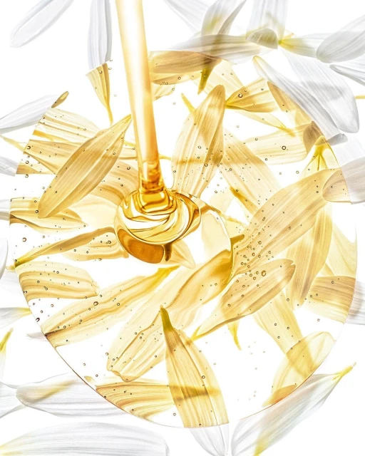 Close-up of golden liquid pouring into a circular frame filled with white and yellow flower petals against a bright white background.