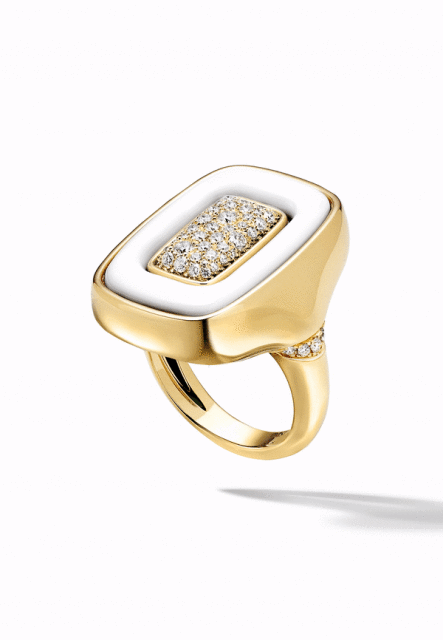 A high-angle, close-up product shot showcases a gold ring with a white enamel face encrusted with diamonds, presented against a seamless white backdrop.