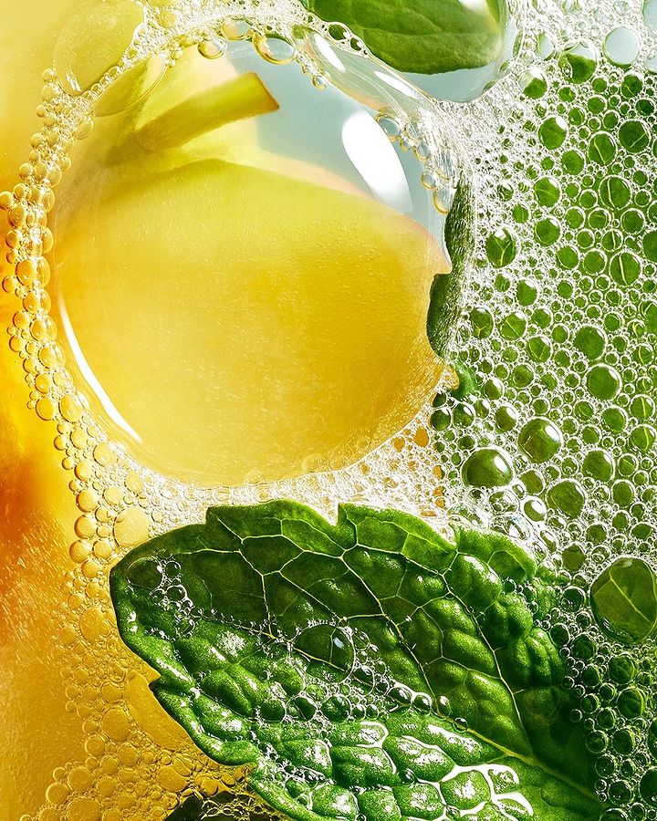 Close-up studio shot showcasing a vibrant composition of a yellow fruit slice, green mint leaf, and water bubbles creating an effervescent scene.
