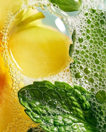 Close-up studio shot showcasing a vibrant composition of a yellow fruit slice, green mint leaf, and water bubbles creating an effervescent scene.