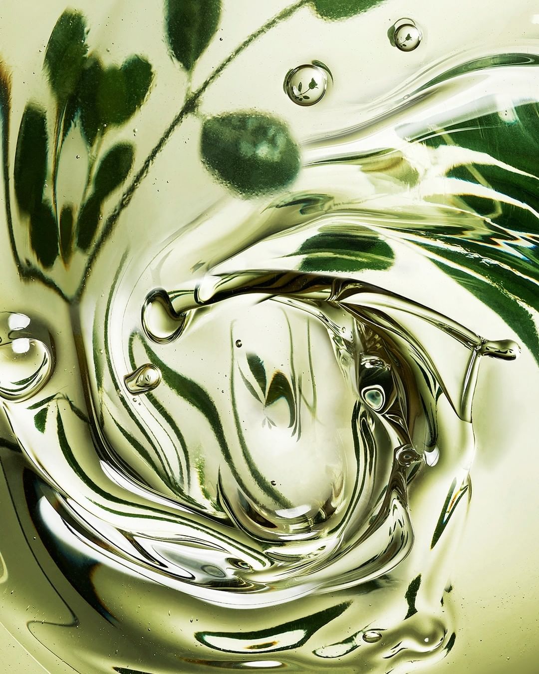 Close-up of clear gel with green leaves suspended, creating a swirling effect, highlighted by a light and airy color palette.