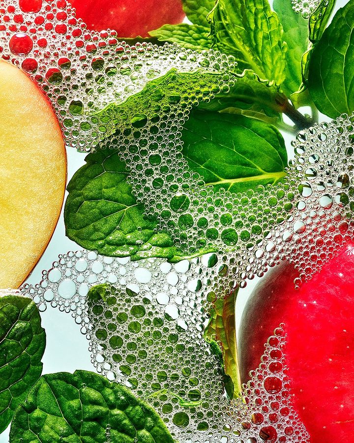 Overhead shot of sliced apples and mint leaves in clear water with scattered bubbles, creating a refreshing and vibrant still life.