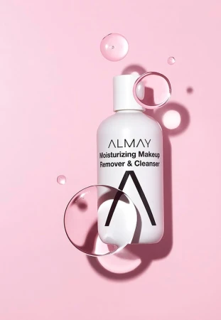 Almay moisturizing makeup remover and cleanser bottle sits on a pink background with several clear, spherical water droplets.