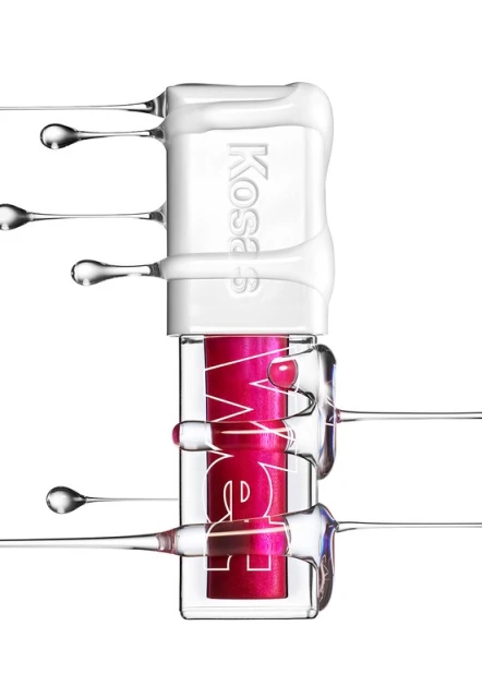 Cosmetic product by KOSAS featuring a tube of lip gloss surrounded by clear liquid and white cream on a bright white backdrop.
