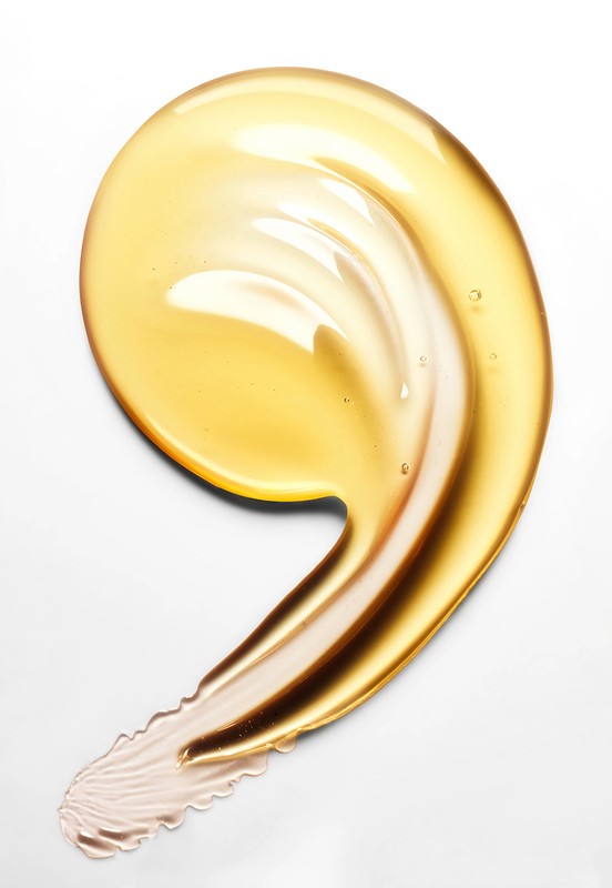 Close-up of a golden yellow cosmetic serum or oil swatch on a white background, showcasing its smooth texture and glossy appearance.