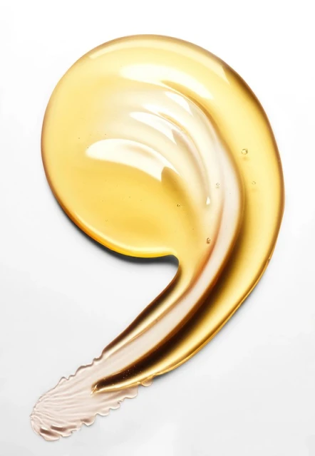 Close-up of a golden yellow cosmetic serum or oil swatch on a white background, showcasing its smooth texture and glossy appearance.