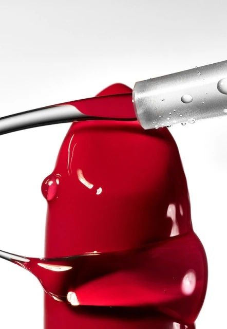 Close-up of red lipstick with a brush applicator, showcasing the texture and color against a clean white background in studio lighting.