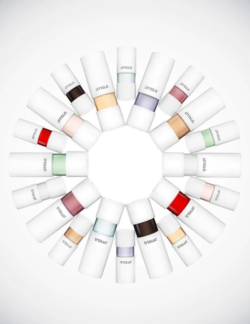 Arrangement of twenty-one white cylindrical cosmetic tubes, each with a different band of color, on a gradient white backdrop.