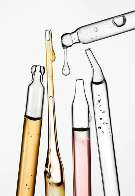 Several transparent glass ampoules filled with different colored serums and an eyedropper with a drop of clear liquid.
