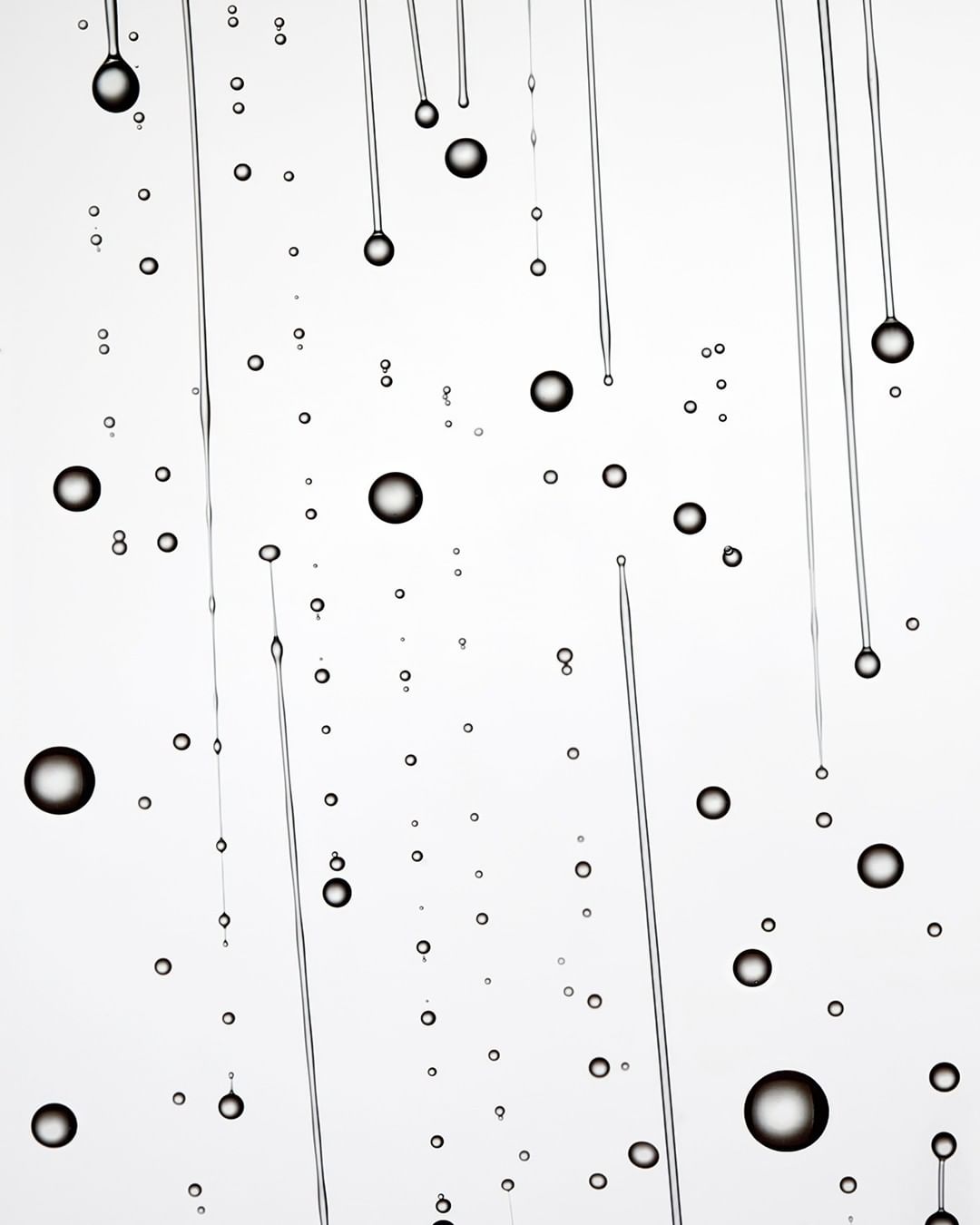 Abstract image of water droplets and thin streams against a bright white background, creating a visually interesting, minimalist composition.