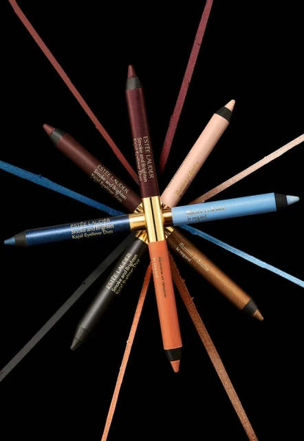 Close-up studio shot of Estee Lauder eyeliner pencils in assorted colors arranged in a radial pattern on a black backdrop.