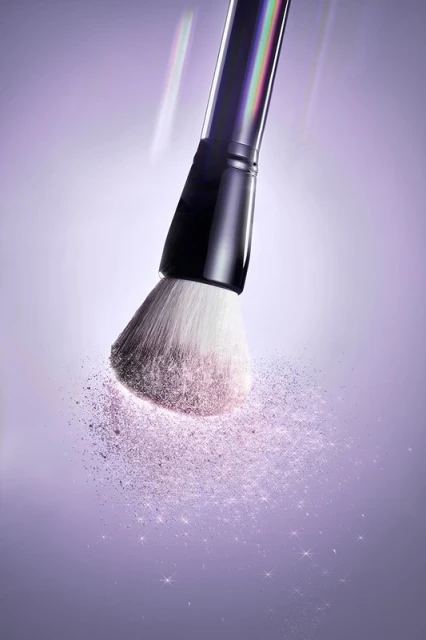 Close-up shot of a makeup brush with powder particles on a lilac background. Beauty and cosmetics product photography.