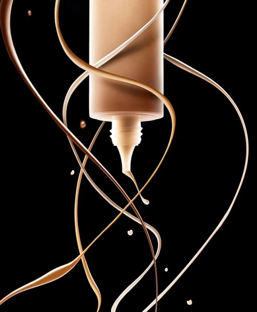 Beige foundation makeup emerging from a tube with streaks of tan and beige liquid against a stark black backdrop in studio shot.