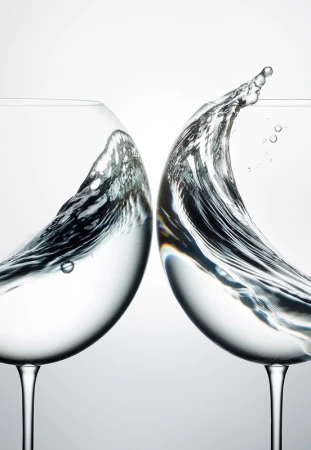 Two wine glasses filled with water capturing dynamic splashes and ripples inside against a clean light background.