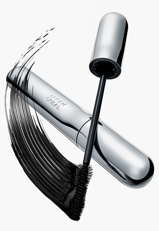 A silver mascara tube and applicator brush are displayed against a white backdrop, with black product swatches nearby.