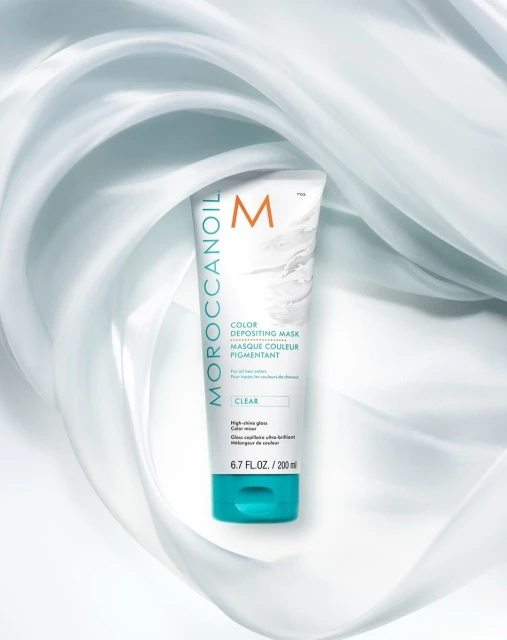Moroccanoil color depositing mask tube on a soft, light blue swirl background. Beauty and personal care product shot.