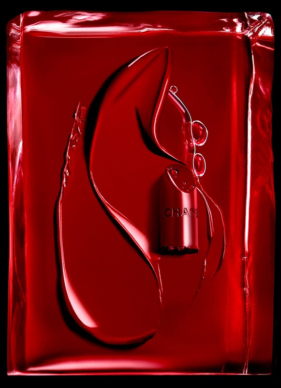 Bold cosmetic still life of red lipstick encased in shiny red gel, dramatically lit against a black background.