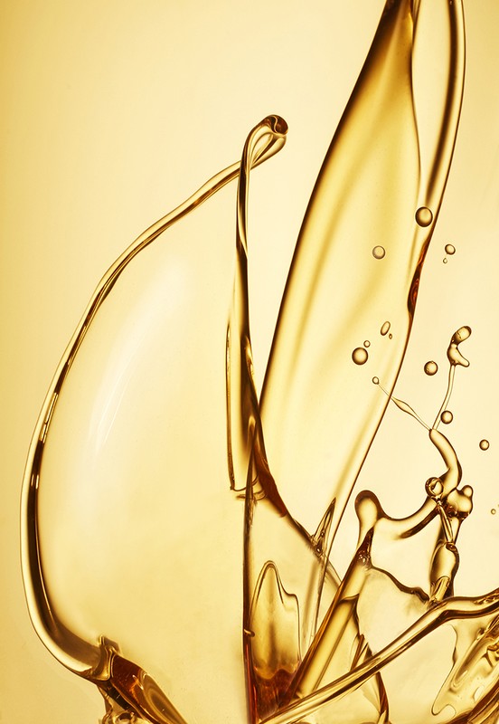 Dynamic close-up of translucent golden liquid splashing against a soft gold background, capturing its viscosity and movement.