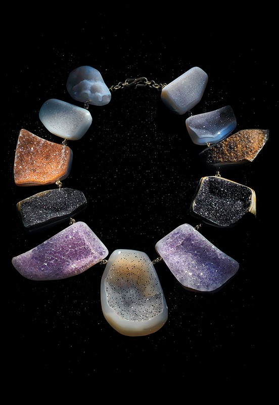 Necklace featuring large, irregular, colorful polished stones connected by a delicate chain against a black, softly speckled background.