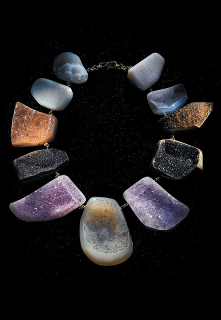 Necklace featuring large, irregular, colorful polished stones connected by a delicate chain against a black, softly speckled background.