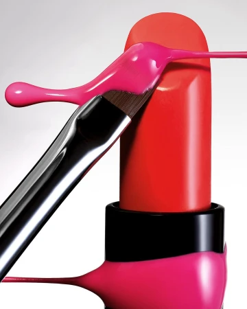 Still life shot of red lipstick with a makeup brush applying pink cream against a white background in vertical format, close-up.