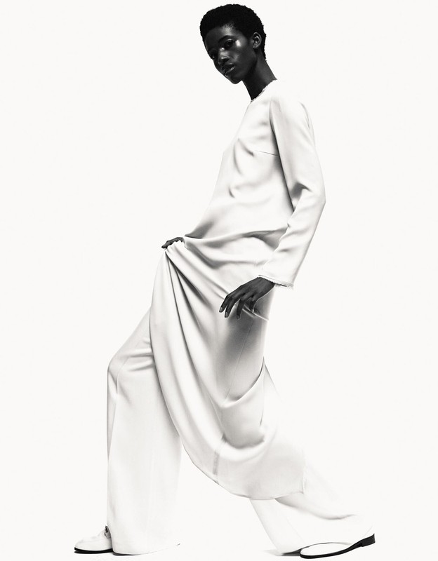 Monochrome fashion shot of a black woman in a light-colored, elegant dress, posing in a bright studio with soft lighting.