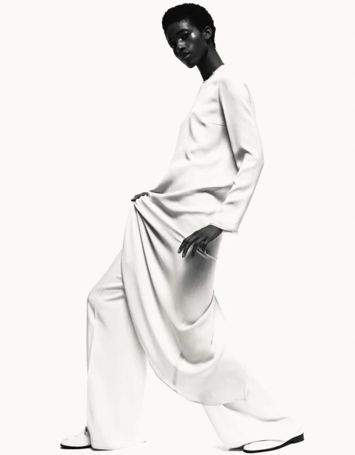Monochrome fashion shot of a black woman in a light-colored, elegant dress, posing in a bright studio with soft lighting.