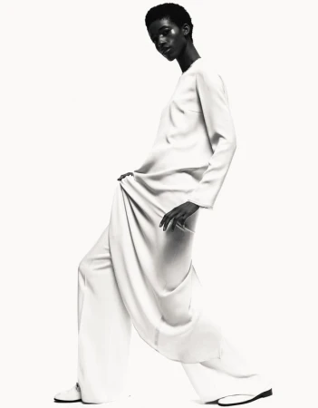 Monochrome fashion shot of a black woman in a light-colored, elegant dress, posing in a bright studio with soft lighting.
