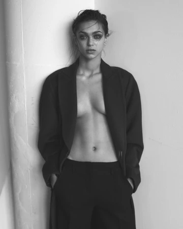Monochrome portrait of a woman leaning against a wall wearing an unbuttoned blazer and trousers.
