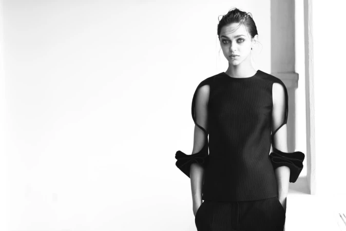 Model in a black structured top with cut-out shoulders standing indoors photographed by Kevin Obrien