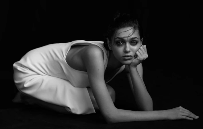 Monochrome portrait of a woman kneeling in a white dress against a dark background, photographed by Kevin Obrien