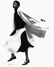 Black model wearing a white coat and black pleated skirt against a bright white background