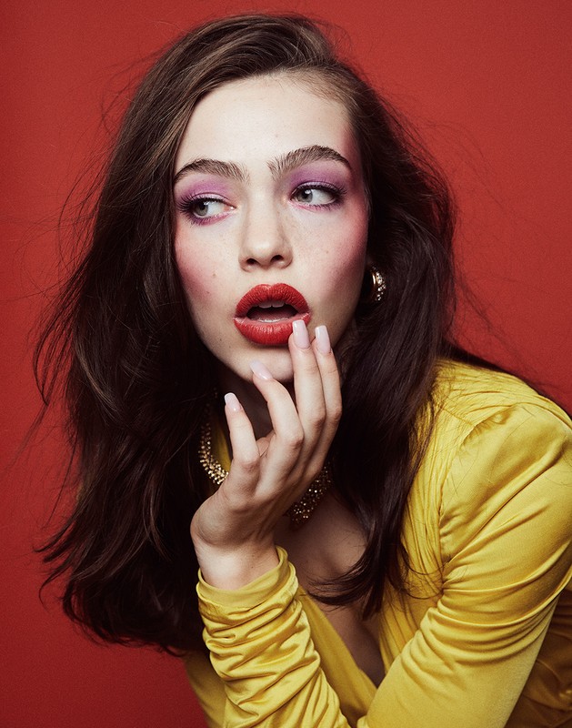Portrait of a woman with pink eyeshadow and red lipstick in a yellow dress against a red background. Beauty shot, makeup and fashion.