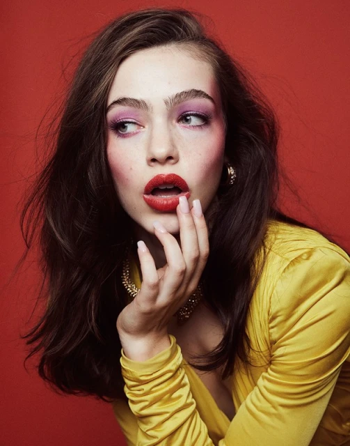 Portrait of a woman with pink eyeshadow and red lipstick in a yellow dress against a red background. Beauty shot, makeup and fashion.