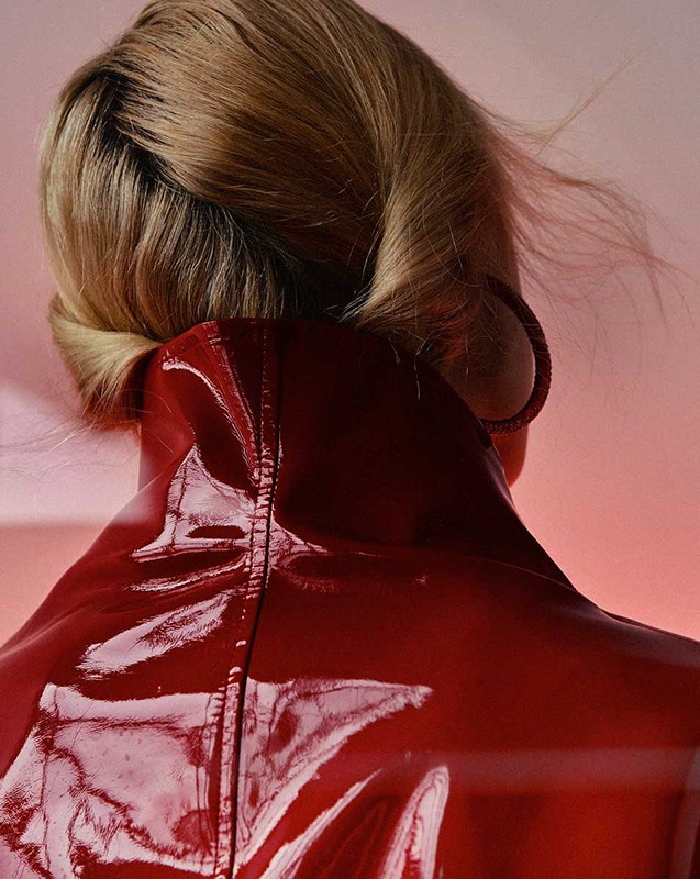 Blonde woman from behind wearing red shiny jacket and hoop earring against pink backdrop in close up portrait. Fashion Beauty.