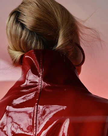 Blonde woman from behind wearing red shiny jacket and hoop earring against pink backdrop in close up portrait. Fashion Beauty.