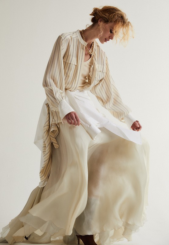 Woman in a striped blouse and flowing layered skirt posing against a plain white studio background.