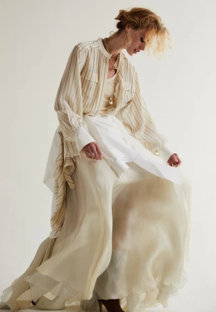 Woman in a striped blouse and flowing layered skirt posing against a plain white studio background.