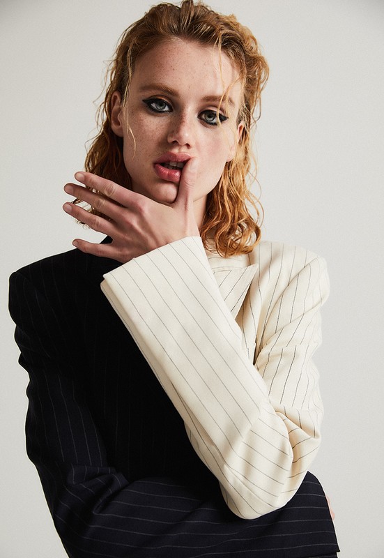 Model with wet ginger hair wearing a two tone black and white pinstripe blazer against a light background