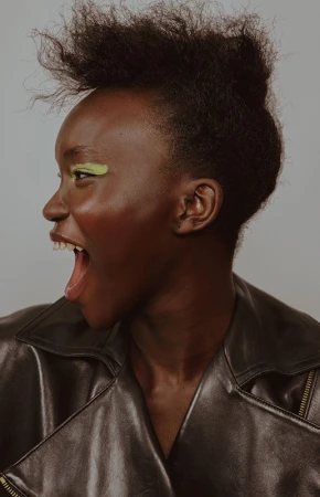 Profile portrait of Black woman with bright green eyeshadow wearing a black leather jacket against a light background