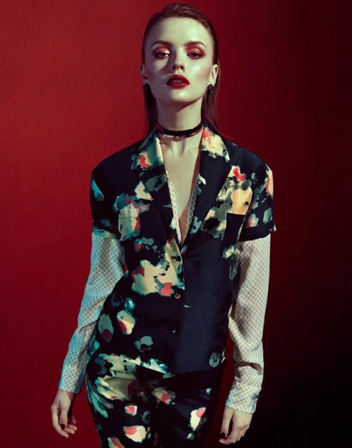 Portrait of a young woman in a printed suit against a red backdrop. Fashion shot featuring makeup and dark floral blazer and pants.