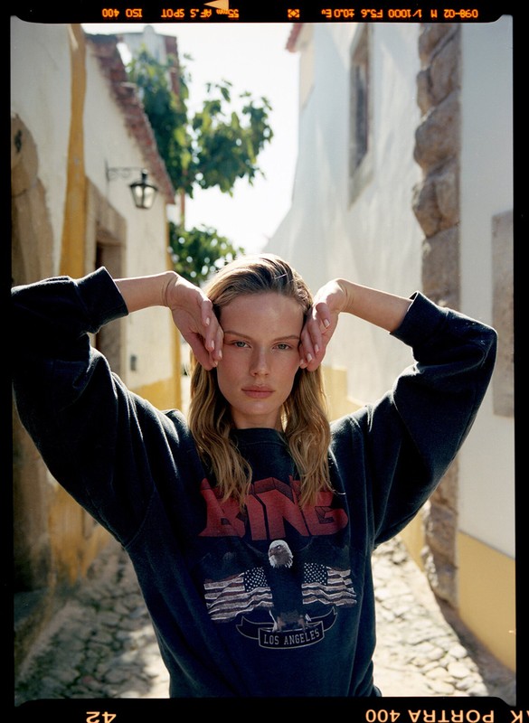 Close-up of a fashionable young adult woman posing outside on a cobblestone street wearing a dark sweatshirt with graphic design.